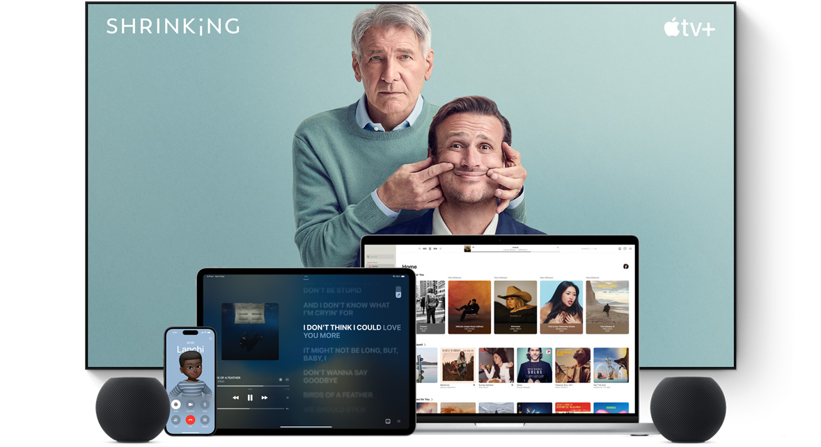 Large flat screen television showing two male characters from the Apple TV+ series shrinking. A MacBook Pro, an iPad, an iPhone and a Midnight HomePod mini are arranged in front.