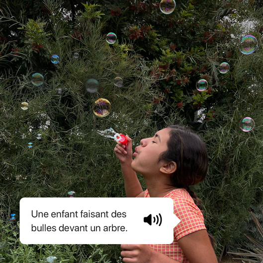 VoiceOver décrivant une photo et affichant la sortie vocale. « Une enfant faisant des bulles devant un arbre. »