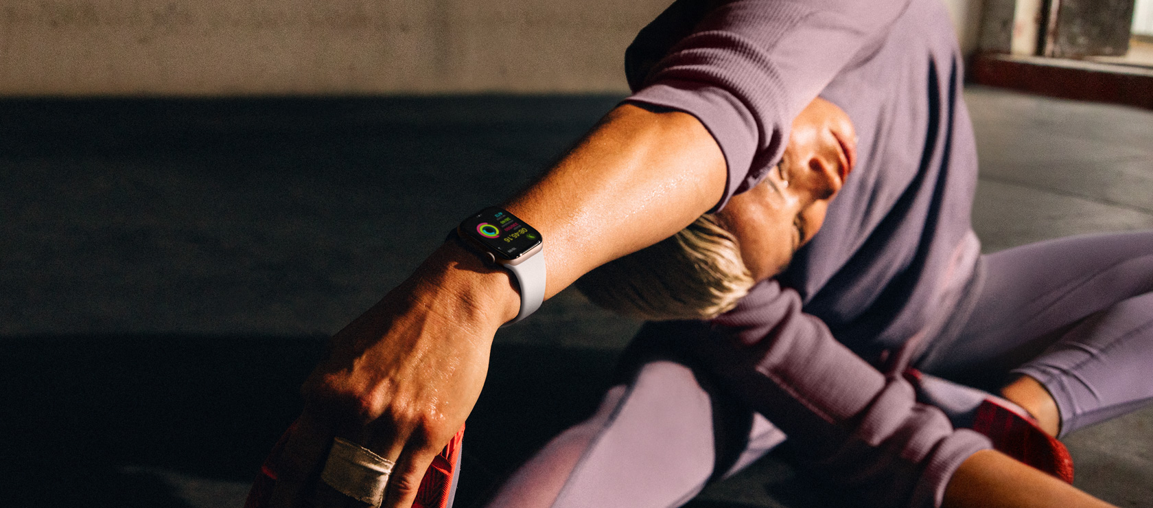 Une femme assise sur le sol étire son bras gauche au-dessus de sa tête vers sa jambe droite; elle porte une Apple Watch Series 10.