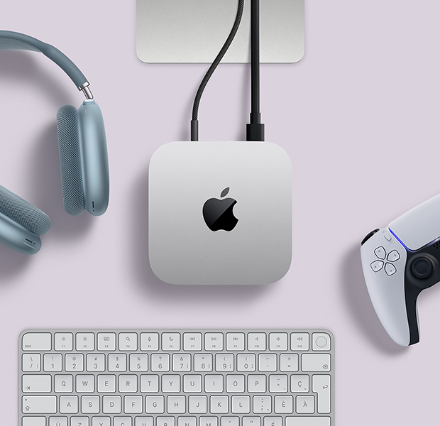 Vue du dessus d’un Mac mini argent, avec deux câbles branchés dans les ports arrière, à côté d’AirPods Max bleus, d’un Magic Keyboard argent et d’une manette de jeu sans fil 