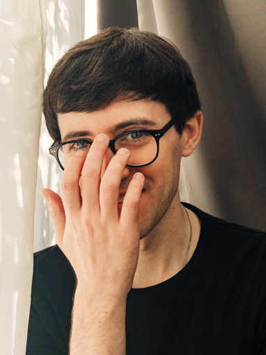 Photo portrait of Matthew, smiling at the reader as he adjusts his eyeglasses.