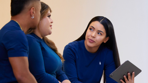 Three Apple Retail employees talking together with one holding an iPad.