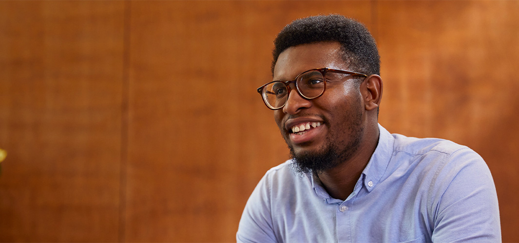 Chidi, seated and smiling, looking off to the side.