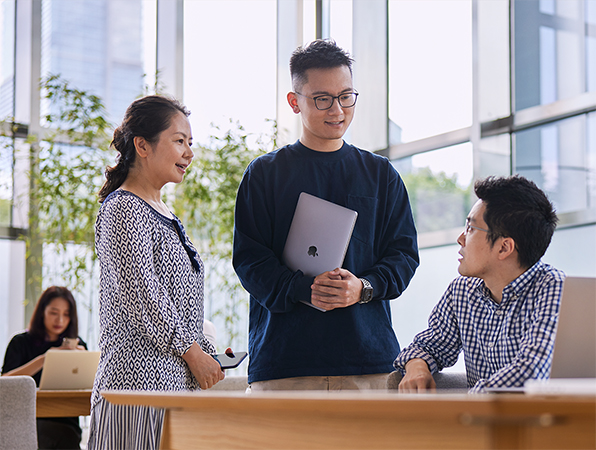 Three Apple Operations and Supply Chain employees talking in a room with floor-to-ceiling windows.