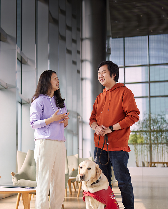 Two Apple employees talking in a bright common area, one holding the leash to a service dog.