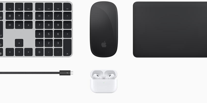 Touch ID搭載のブラックのMagic Keyboard、ブラックのMagic Mouse、ブラックのMagic Trackpad、ブラックのアクセサリコード、蓋の開いたホワイトの充電ケースに収められたホワイトのAirPodsなどの様々なMacのアクセサリ