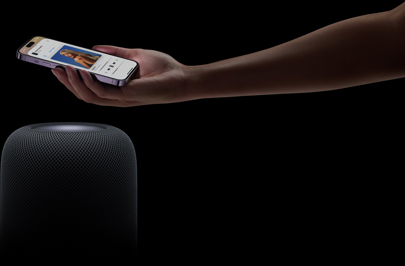 A hand coming in from the right side of the page holds an iPhone above a HomePod speaker