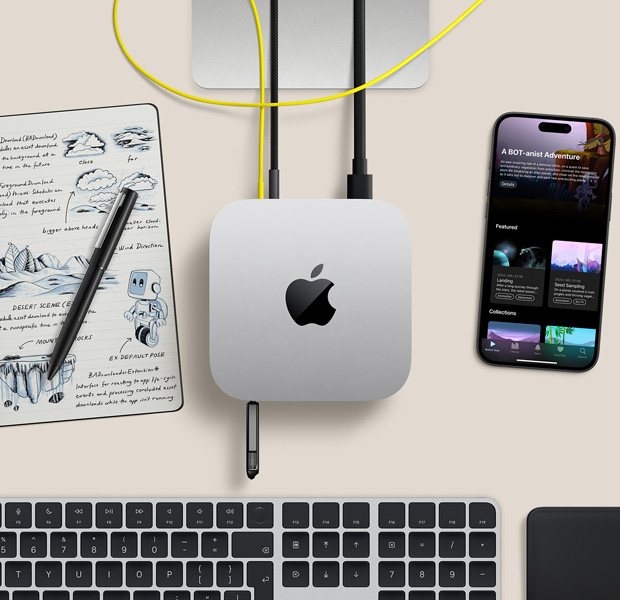 Pohľad zvrchu na strieborný Mac mini na stole s káblami a flash diskom zapojenými do portov. Vedľa leží bezdrôtová klávesnica, trackpad, iPhone a zošit.